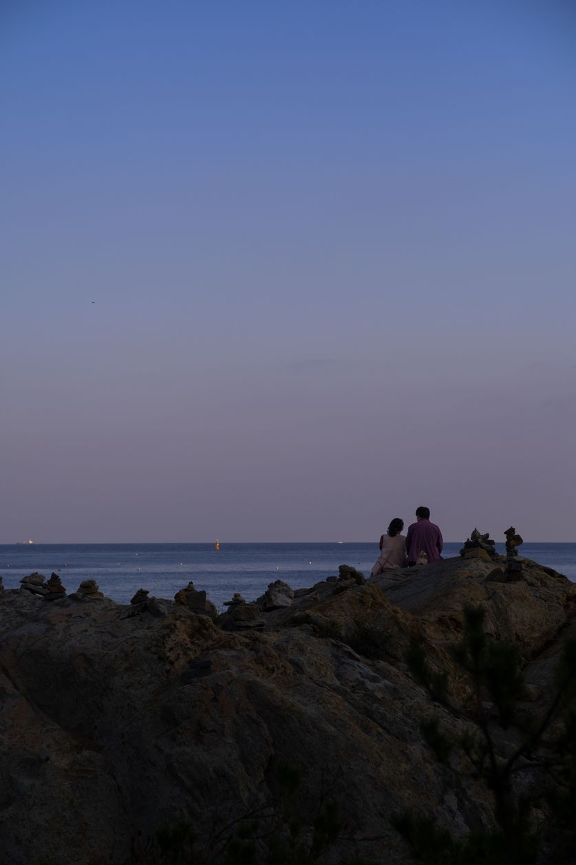 A couple enjoys the onset of evening amidst small towers of carefully placed pebbles.